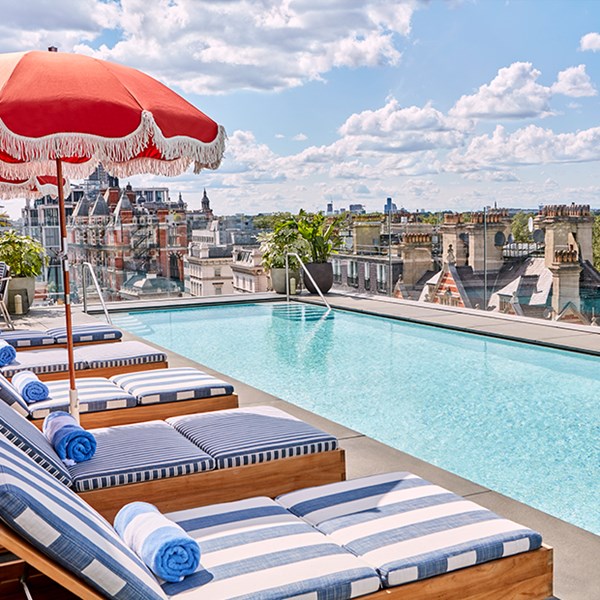 The rooftop pool and bar at The Berkeley with blue and white striped sun loungers, shaders and a view on Hyde Park and the London rooftops